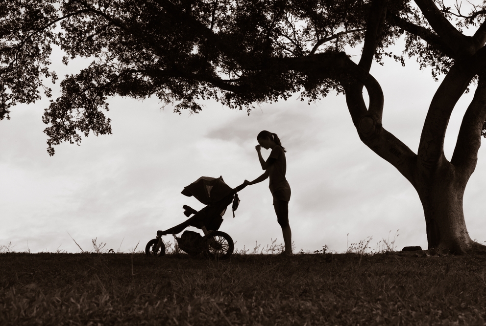 black and white image of woman pushing a baby carriage, with her hand to her brow