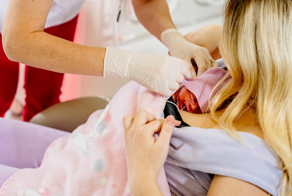 gloved hands attending to baby laying on woman&#039;s chest