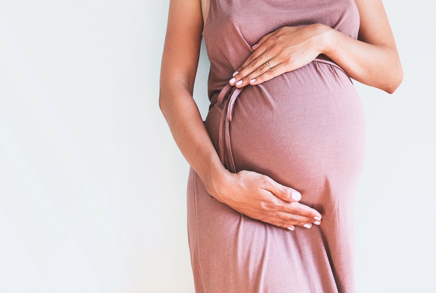 Pregnant woman wearing a pink dress with her hands over her belly