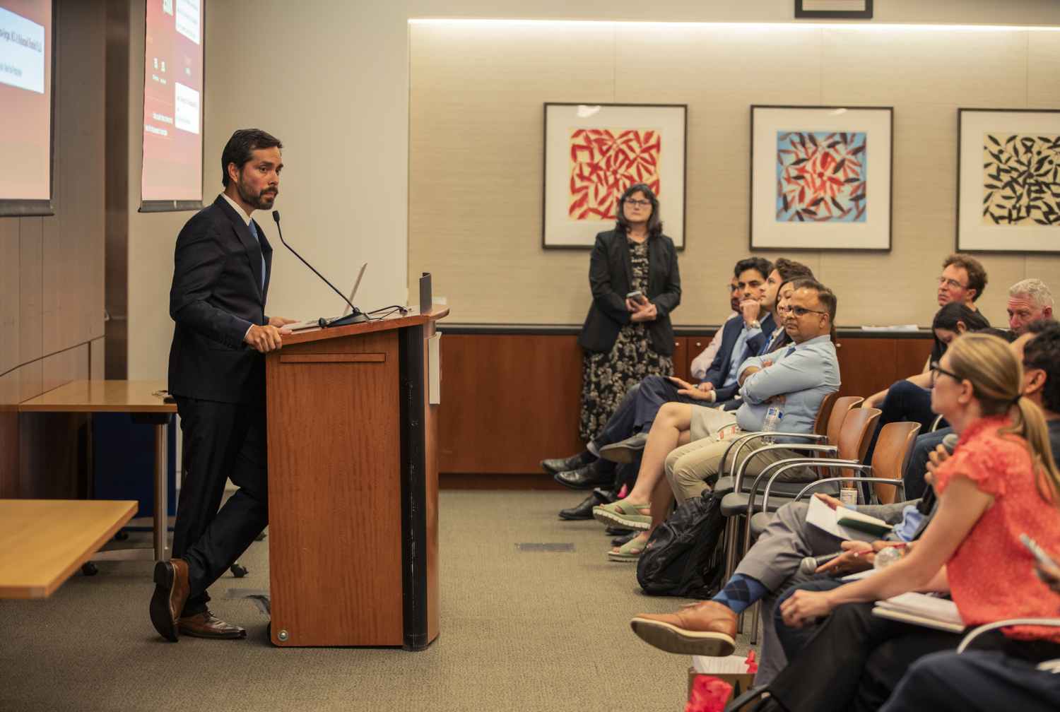 A man wearing business attire is speaking at a podium in front of an audience. 