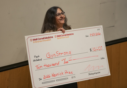 South Asian woman wearing glasses and holding a big check for $10,000