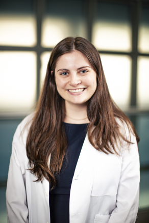 A woman wearing a white coat poses for a photo