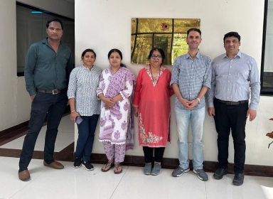 Six people in front of a white building with a gold plaque on it