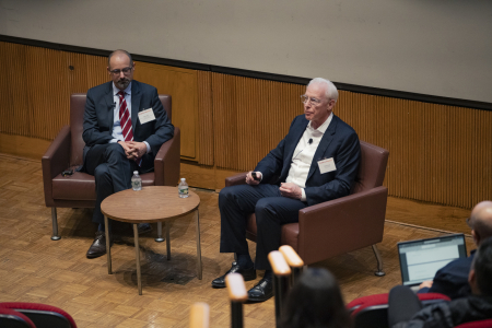Two Caucasian men in business attire talking to an audience in a auditorium