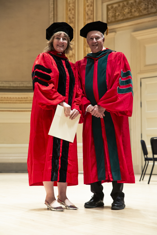 A woman in graduation regalia poses with an administrator as she crosses an ornate stage