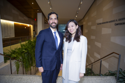 A white Hispanic man with a beard in a dark blue suit and an East Asian woman with long hair wearing a gray dress