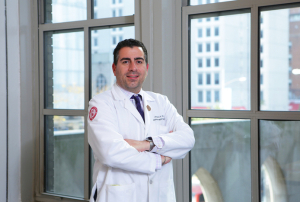A man in a white coat standing next to a window