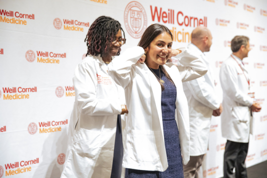 A doctor puts a white coat on a medical student.