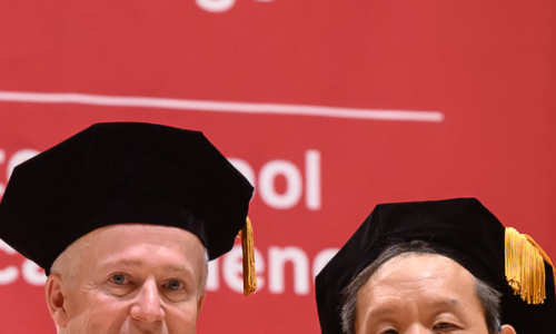 Two men wearing graduation regalia posing during commencement exercises.