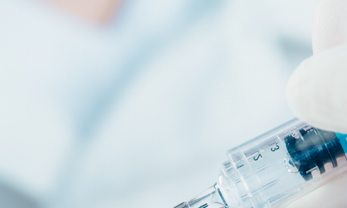photo of a gloved hand inserting a syringe into a vial