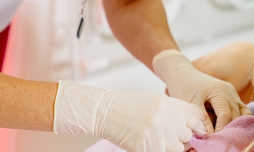 gloved hands attending to baby laying on woman&#039;s chest